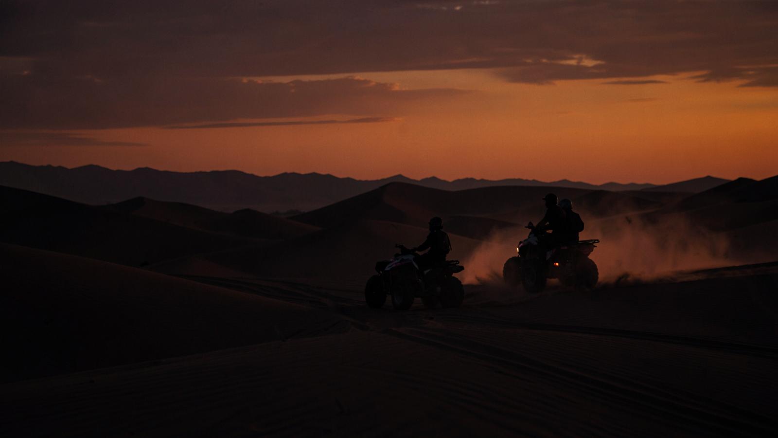 Riders crossing desert dunes at dusk